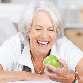 Parodontitis: Lächelnde ältere Frau mit schönen Zähnen hält Apfel